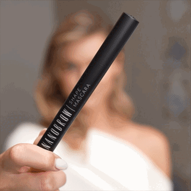 Γαλανομάτα γυναίκα σε λευκό φόρεμα που εφαρμόζει τη Shape Mascara